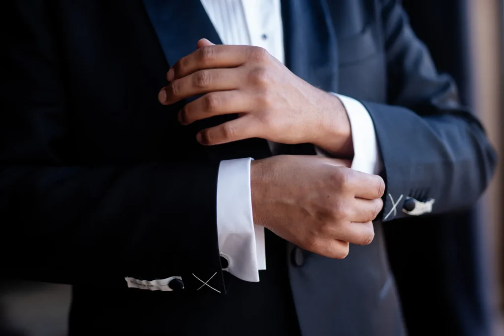 Groom fastening his cufflink in a black suit, luxury Morocco destination wedding detail photography