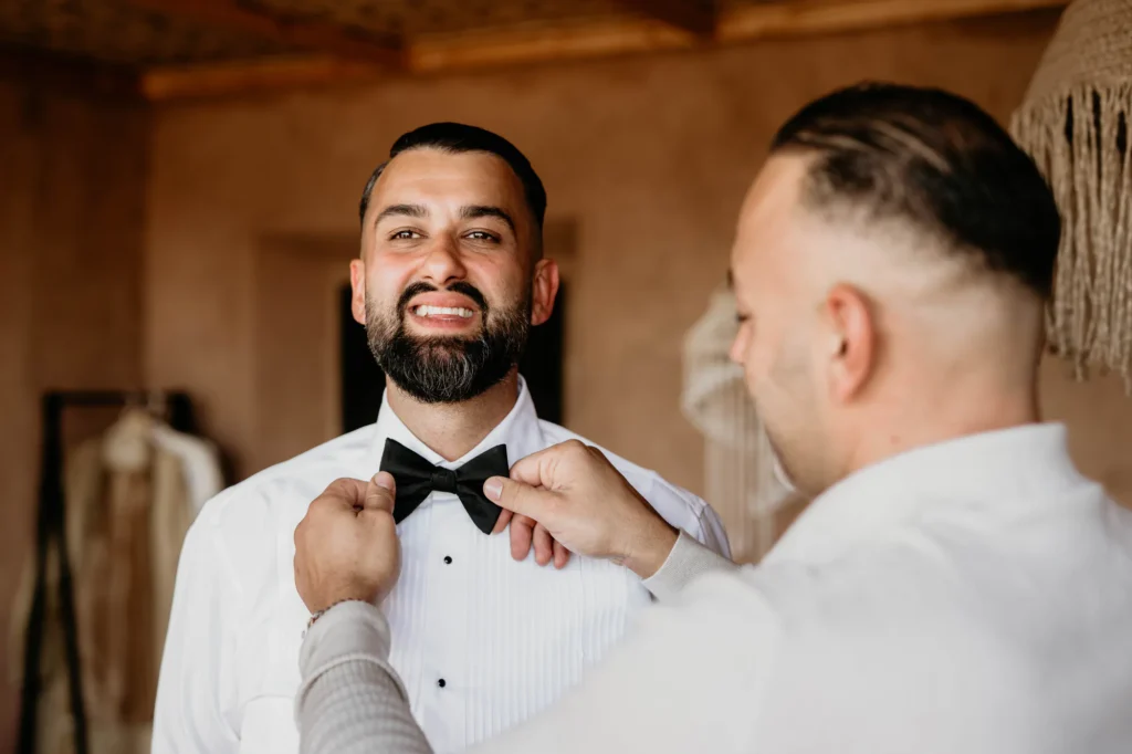 Groom having his black bow tie adjusted before a Morocco destination wedding for European couples
