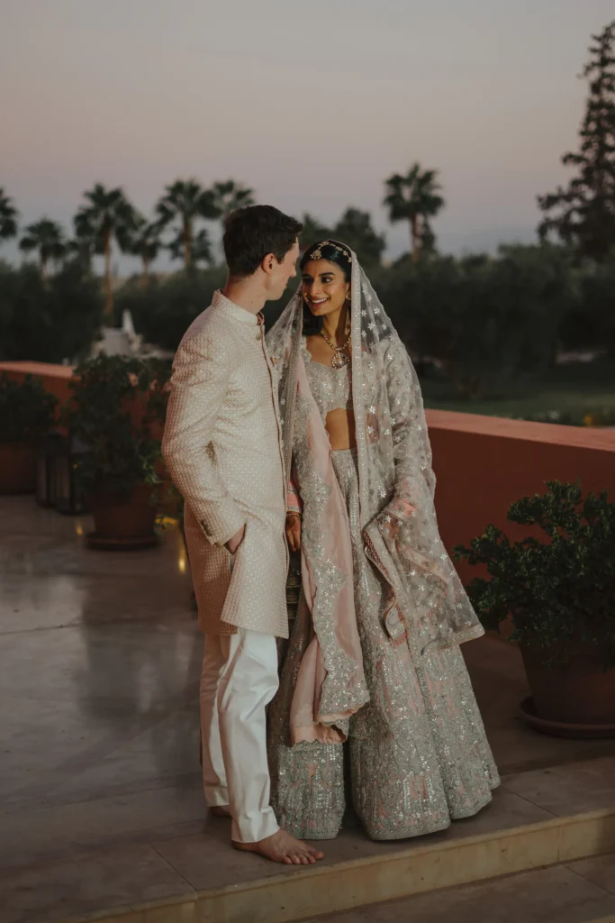 Indian bride and groom in ivory outfits on a rooftop terrace at sunset, Marrakesh destination wedding
